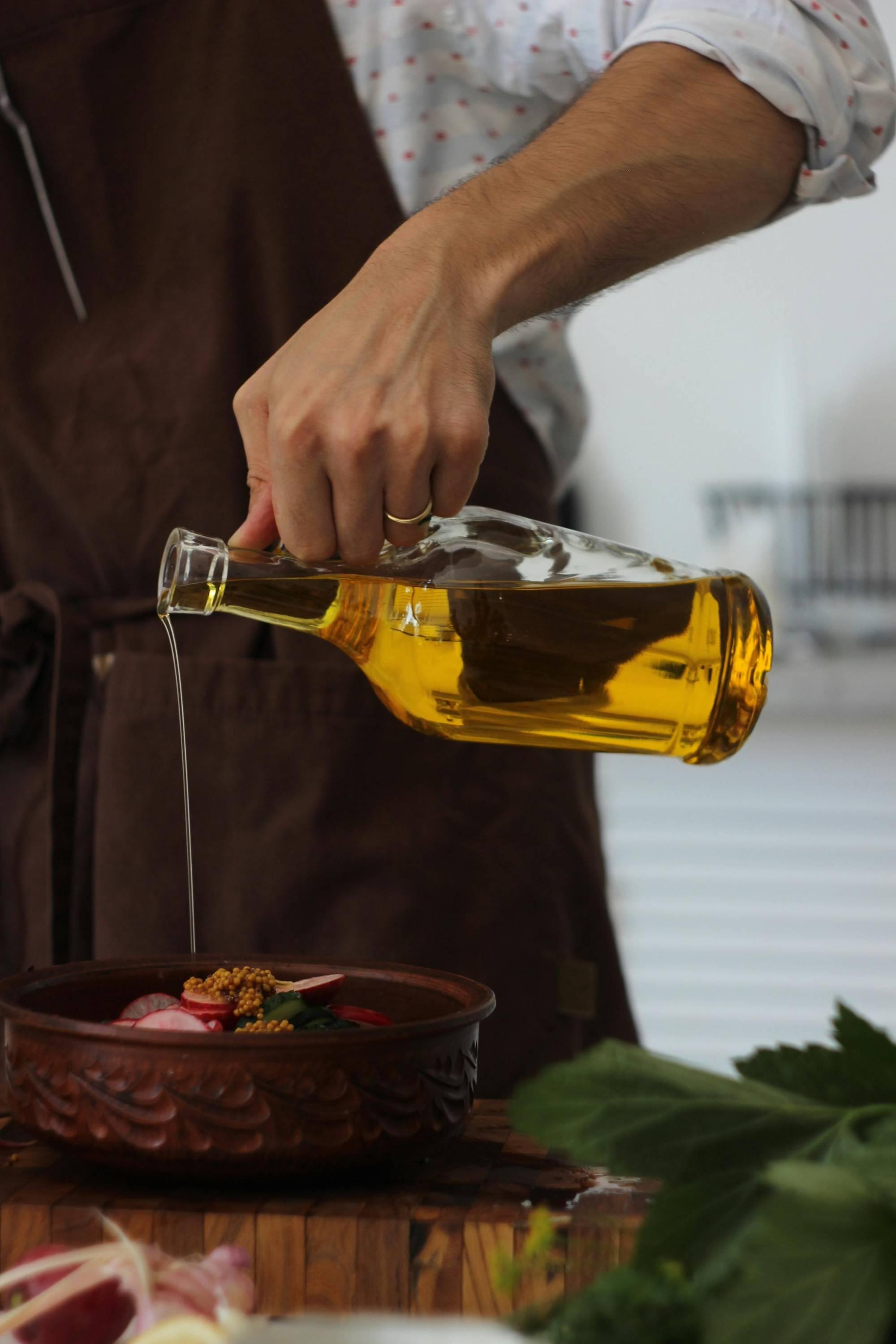 Hand pouring clear glass bottle of olive oil into food dish